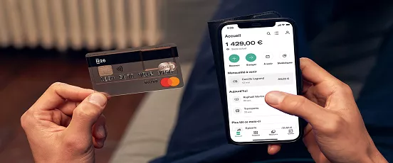 Personne tenant une carte N26 et un smartphone affichant l’application bancaire avec solde et transactions visibles
