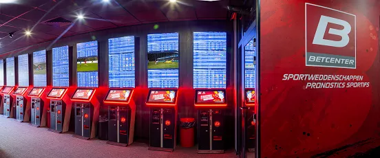 Salle de paris sportifs Betcenter avec bornes interactives rouges et écrans affichant les cotes en direct